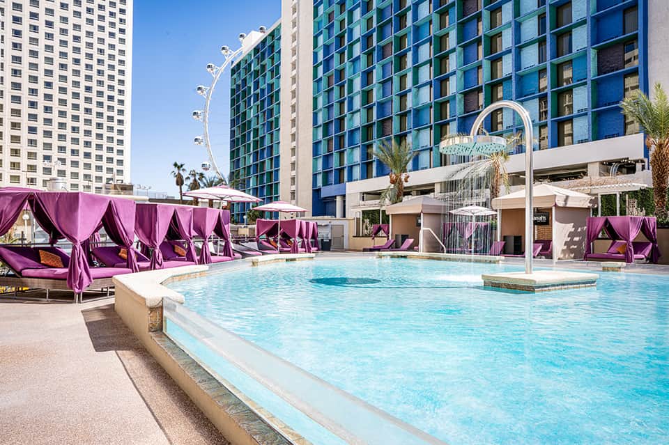 Large resort pool with purple cabanas, high-rise buildings, and sunny poolside seating