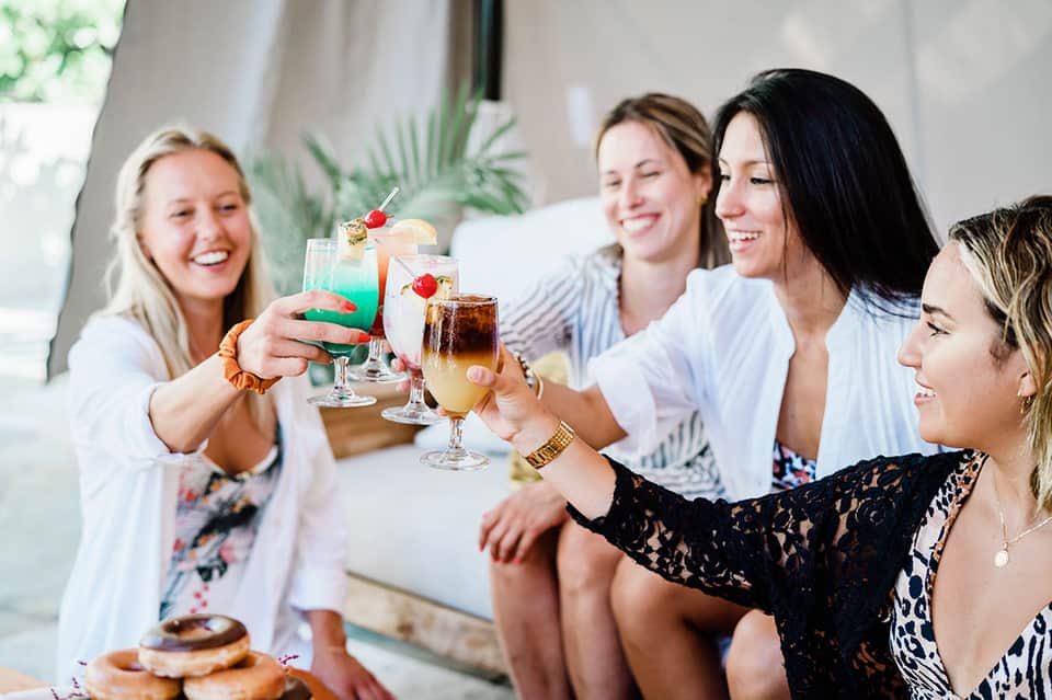 Group of women toasting colorful cocktails at a tropical poolside gathering