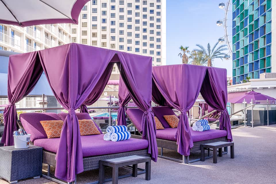 Purple canopy cabanas with cushioned lounges by pool overlooking high-rise hotels