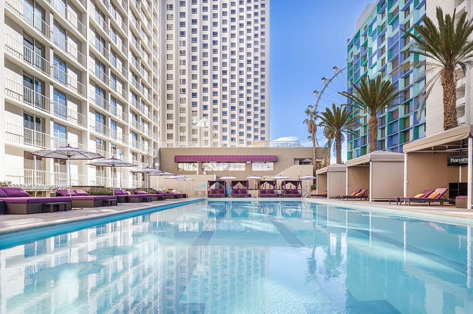Resort pool surrounded by tall buildings and palm trees with purple lounge chairs