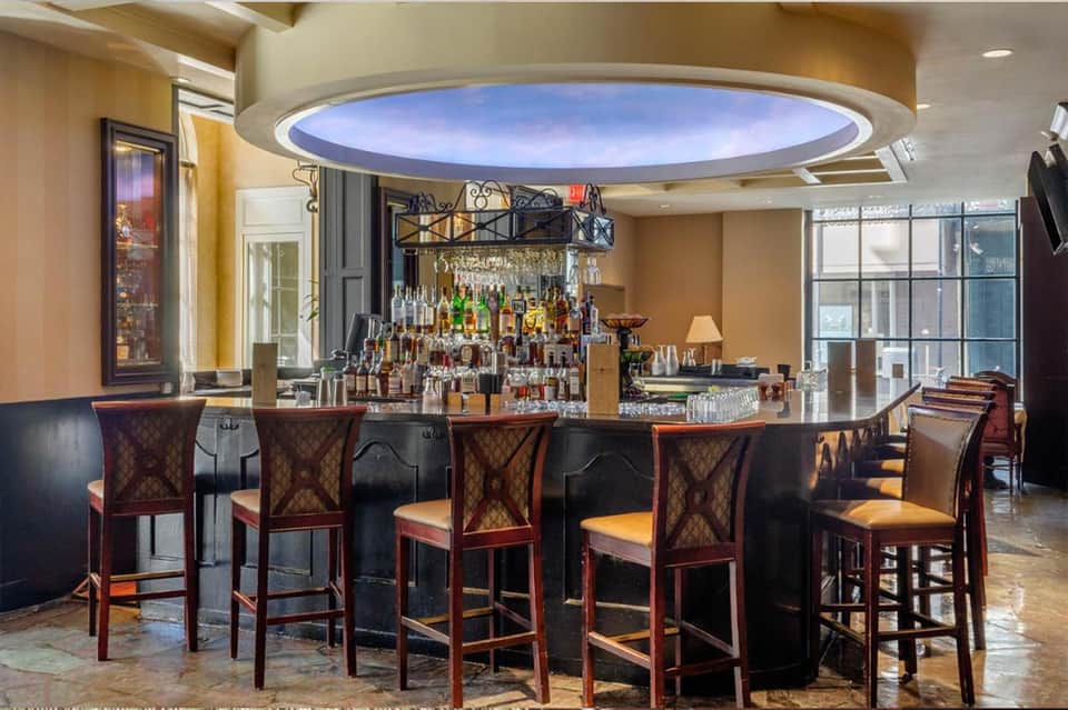 Elegant bar with dark counter, wooden chairs, bottle display, and skylight ceiling