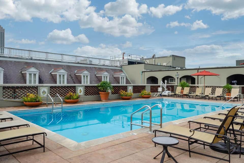 Rooftop outdoor pool with lounge chairs, decorative lattice fence, and mansard-roof building beyond