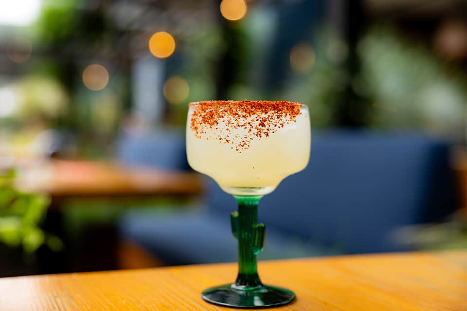 Pale yellow cocktail with cinnamon sugar rim in green-stemmed glass on wooden table