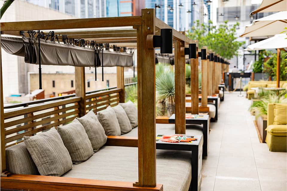 Outdoor lounge area with wooden pergolas, gray cushioned seating, and urban skyline view