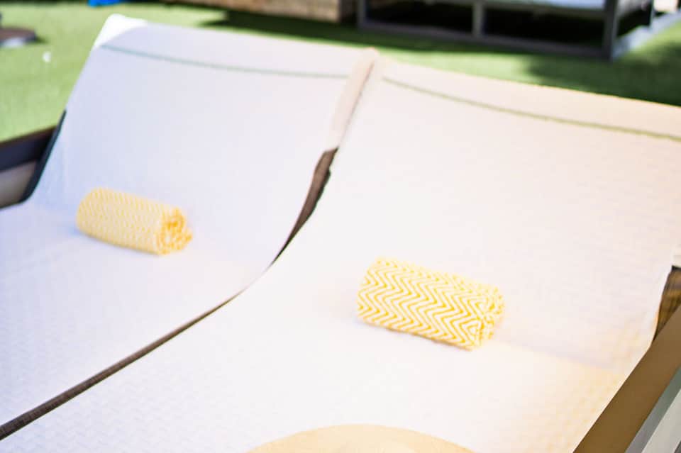 Close-up of two white lounge chairs with yellow and white patterned cushions on grass