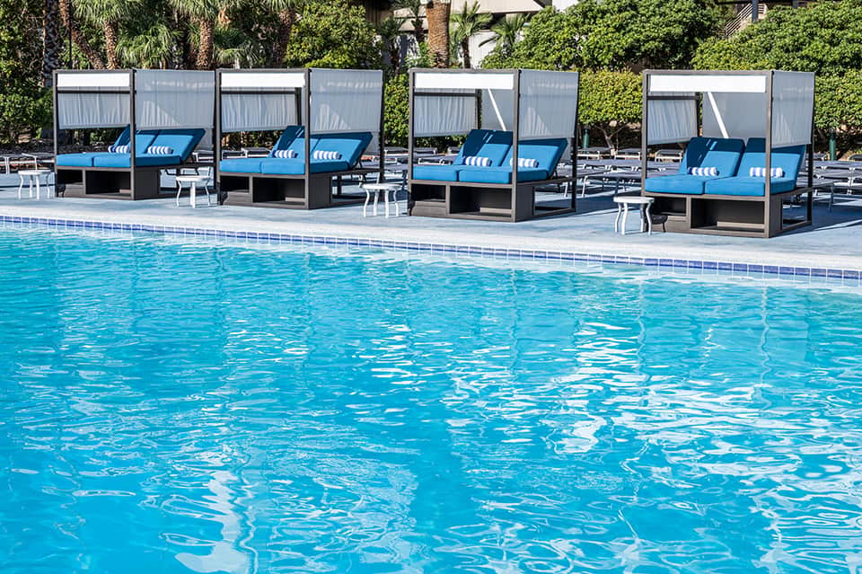 Resort pool with bright blue water and modern cabana loungers with shade structures and palm trees