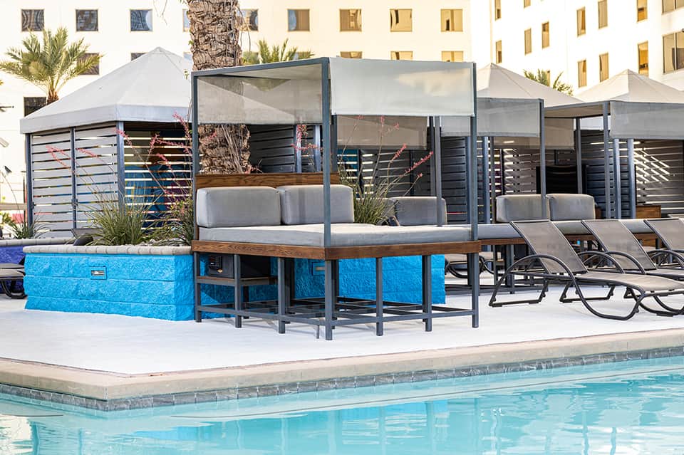 Poolside cabanas with blue accents and gray lounge seating under white tent canopies