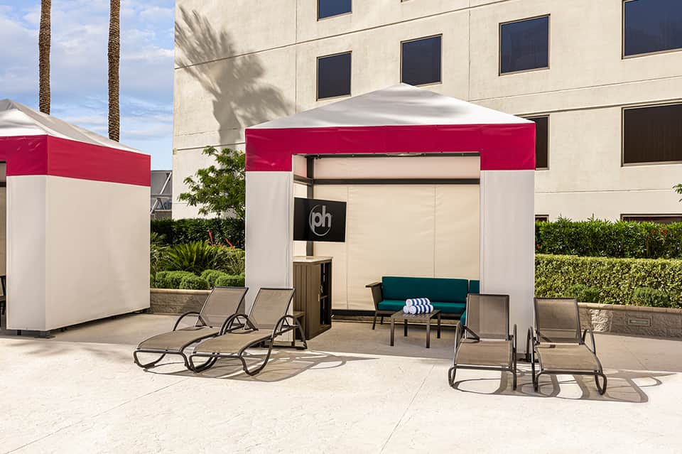 Outdoor patio with red and white cabana tent, lounge chairs, and modern hotel building