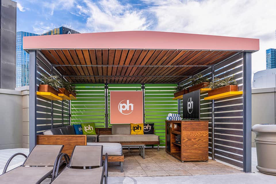 Modern rooftop lounge with green neon lighting, wooden accents, and pink canopy