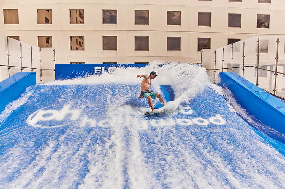 Indoor surfing facility with person riding artificial wave in blue pool with foam