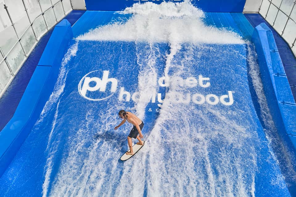 Man surfing on artificial wave pool with branded logo at indoor water sports facility