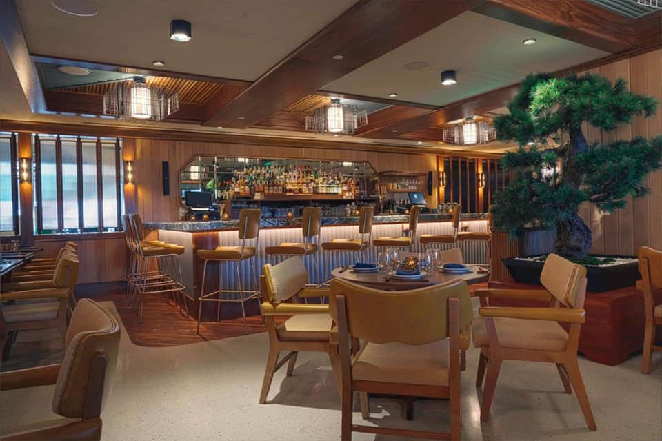 Upscale bar lounge with wood paneling, bonsai tree, leather seating, and well-stocked liquor shelves