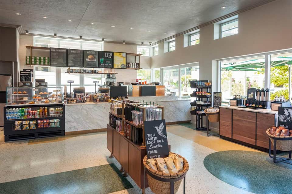 Modern hotel café interior with marble counters, menu boards, and bright windows overlooking a patio area