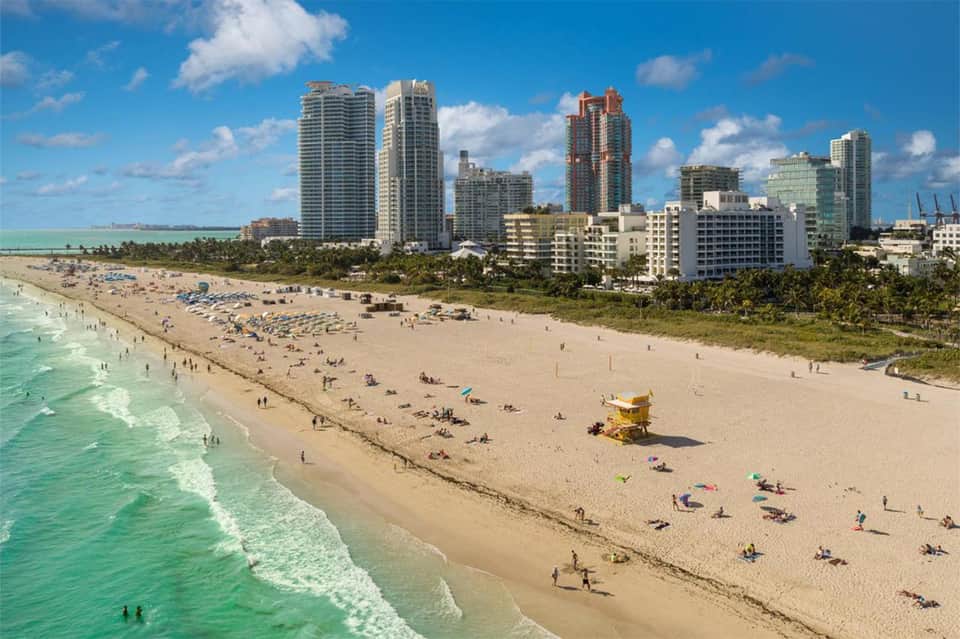 Aerial view of Miami Beach with turquoise ocean, sandy shore, and high-rise hotels under blue sky