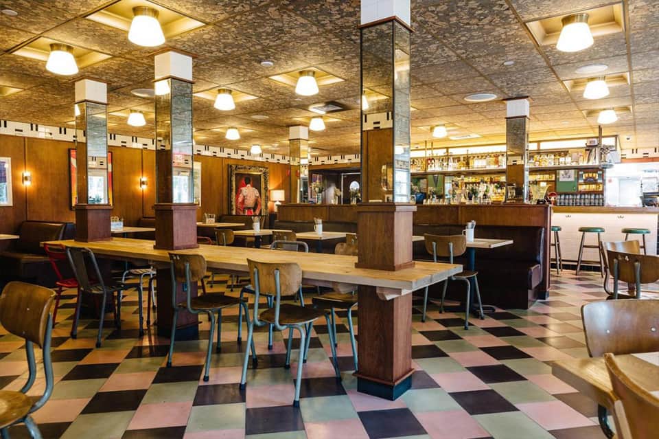 Retro mid-century hotel dining area with wooden booths, colorful checkered floor, and warm ceiling lights