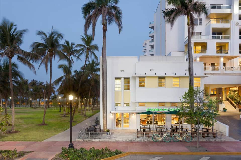 Modern white hotel building with Starbucks café, palm trees, and manicured green lawn at dusk