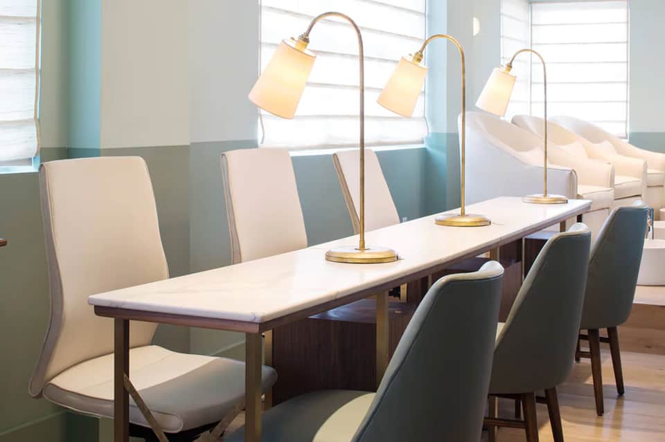 Modern dining room with long white table, brass arc lamps, and upholstered chairs by large windows