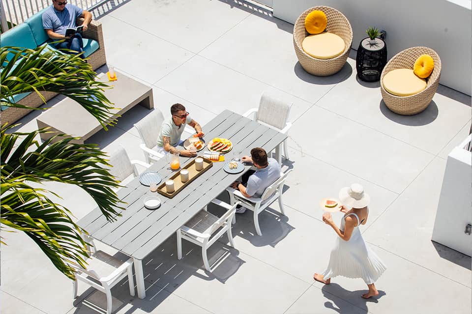 Overhead view of guests dining at an outdoor table on a white patio with woven lounge chairs