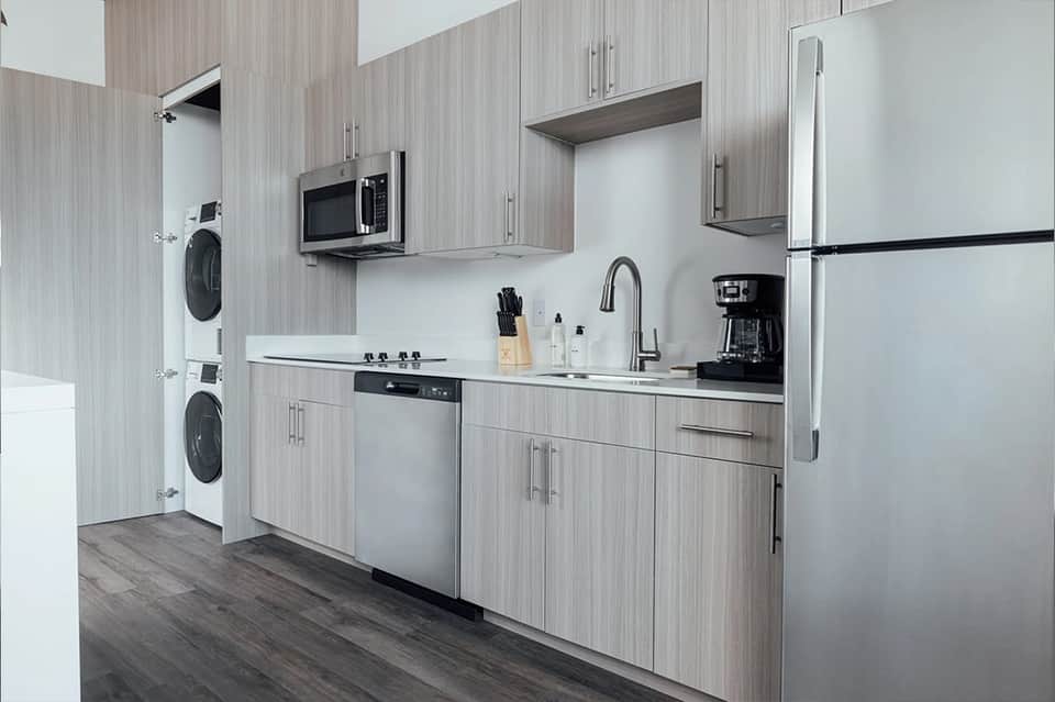 Modern kitchen with gray wood cabinetry, stainless steel appliances, and stacked washer/dryer units