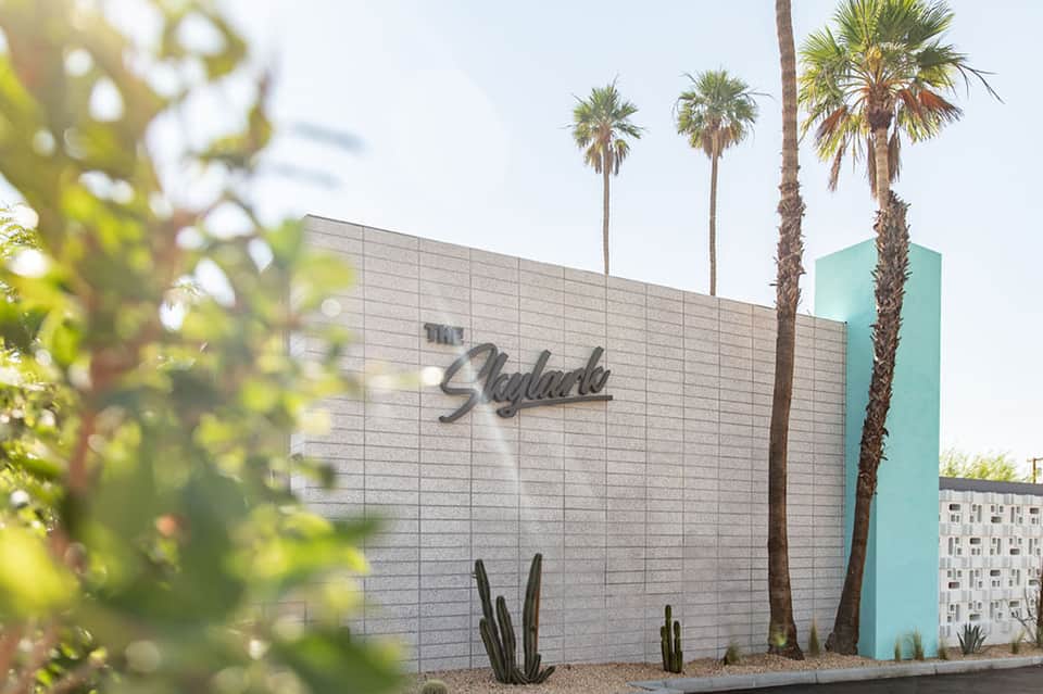 Modern hotel building exterior with 'Skylarke' signage, white brick facade, turquoise accent, and palm trees