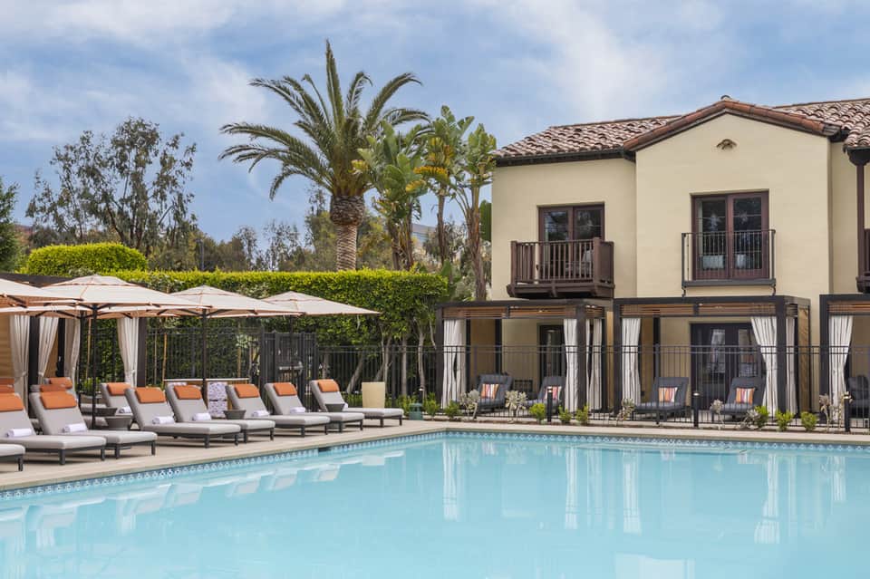 Luxury resort pool with cabanas, palm trees, and cream-colored mansion-style building