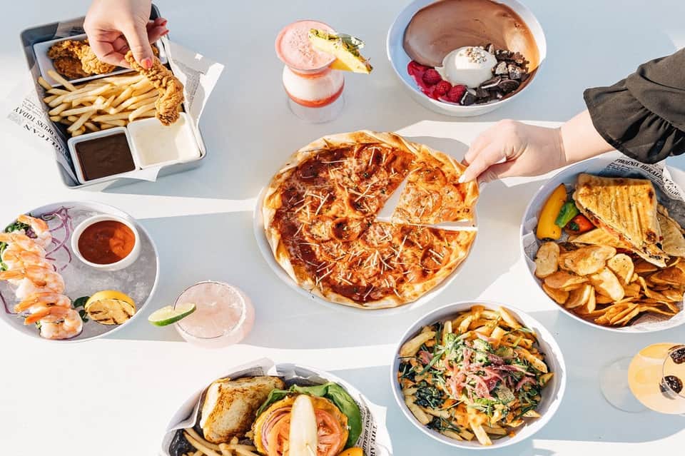 Overhead view of casual dining spread including pizza, fried chicken, appetizers, and desserts
