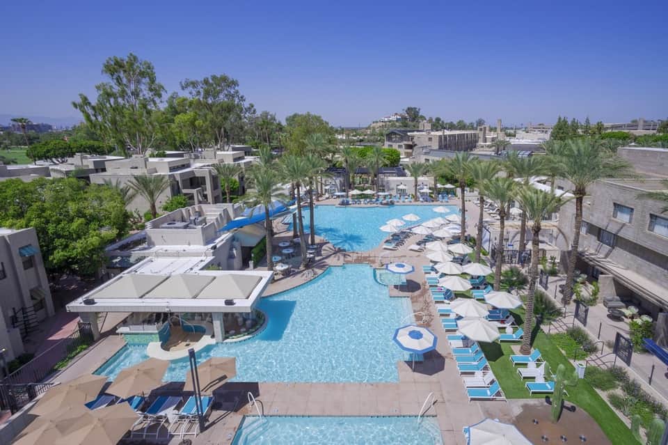 Large resort pool complex with palm trees, multiple loungers, and surrounding residential buildings