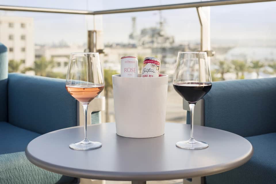 Rooftop lounge with wine glasses and cityscape view, featuring rosé and red wine with canned beverages