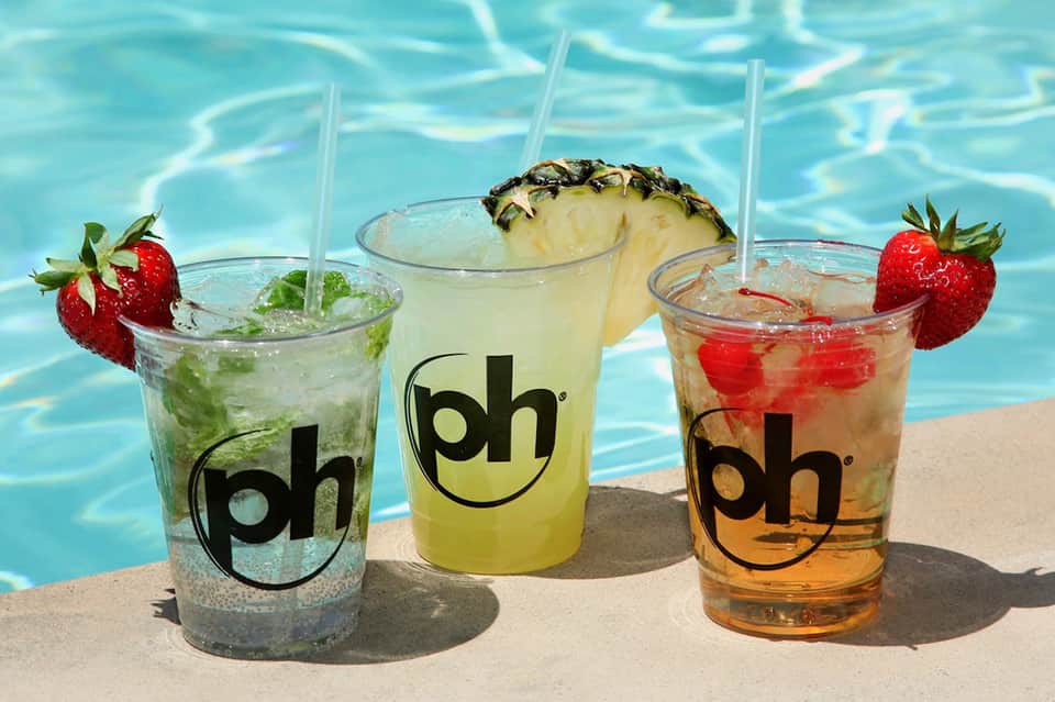 Three colorful cocktails with fresh fruit garnishes by a bright blue swimming pool