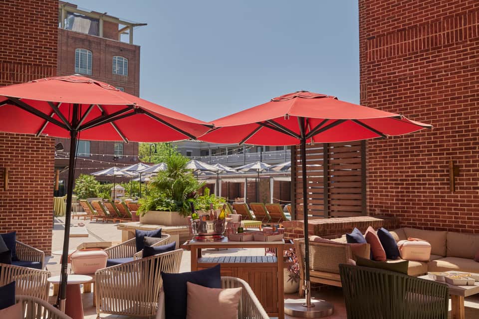 Rooftop terrace with red umbrellas, wicker seating, and brick building backdrop