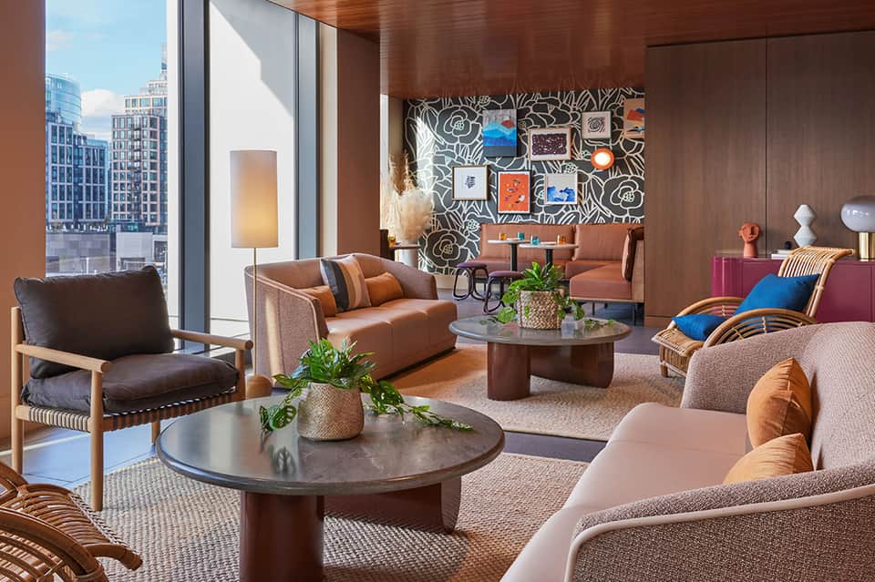 Modern high-rise hotel lounge with brown leather seating, colorful wall art, city skyline views through floor-to-ceiling windows