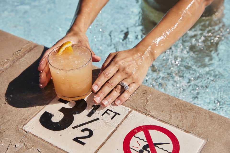 Poolside cocktail with lemon garnish and depth marker sign at pool edge