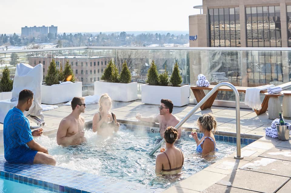 Guests relaxing in hot tub on rooftop terrace overlooking snowy winter landscape