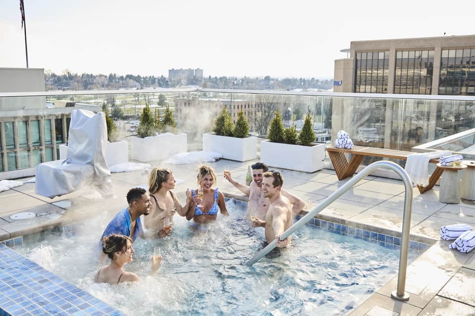 Group of guests relaxing in hot tub on rooftop terrace with city skyline views