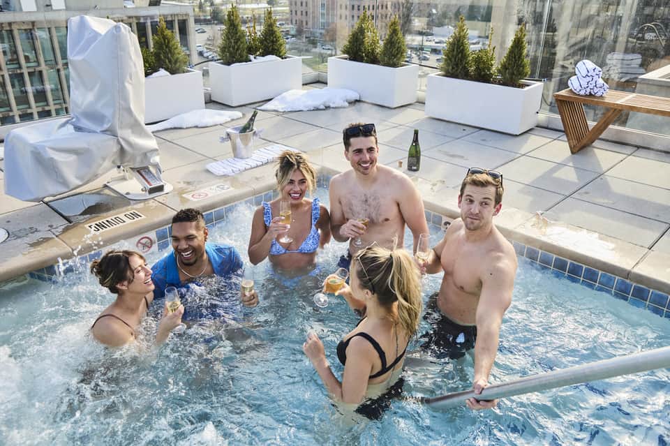 Group of young adults enjoying rooftop hot tub with city skyline and downtown buildings in background