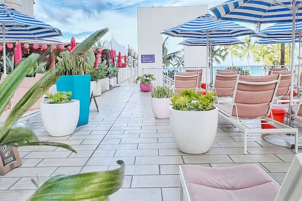 Rooftop terrace with blue striped umbrellas, white planters, pink loungers, and ocean views