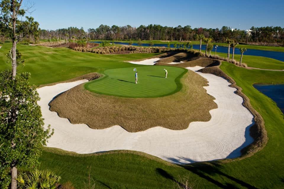 Championship golf course hole with sand bunkers, green fairway, and blue water hazard surrounded by palm trees