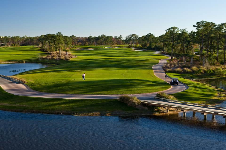 Scenic golf course with pristine fairways, water hazards, and tree-lined landscape with golfers and cart