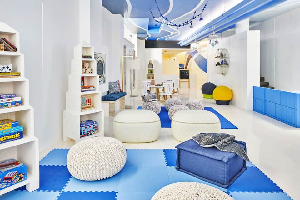 Bright, modern children's play area with blue and white padded flooring, bean bags, storage shelves, and play equipment