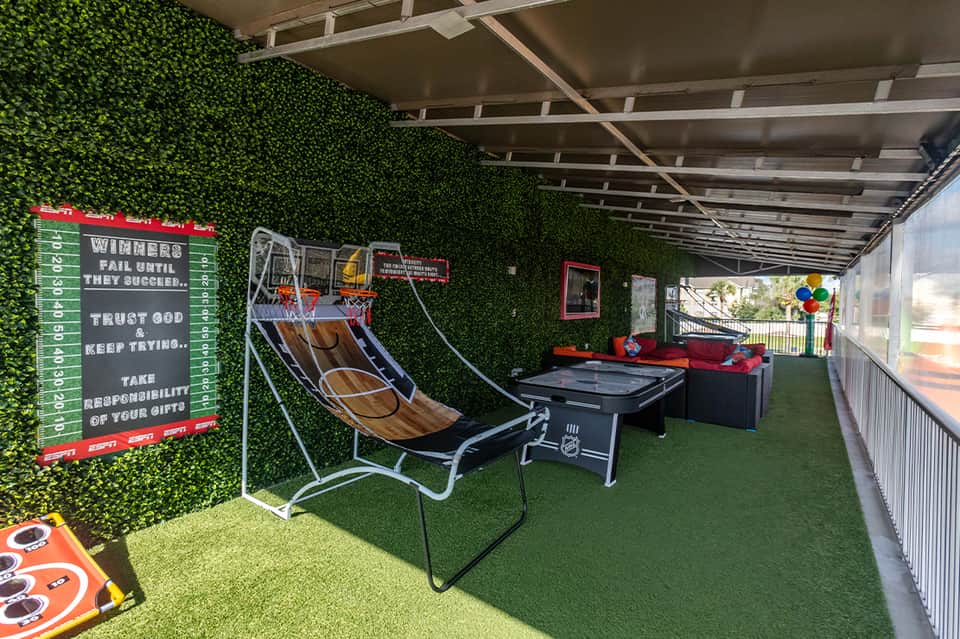 Recreation room with artificial turf, arcade games, basketball hoop, and sports equipment