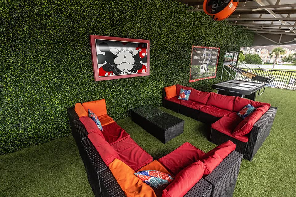 Outdoor lounge area with artificial turf, red cushioned seating, and Mickey Mouse artwork