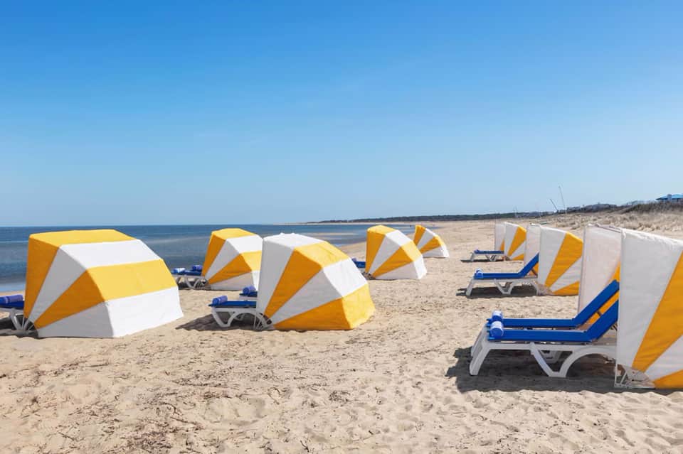 Sandy beach with yellow and white striped umbrellas and blue loungers facing the ocean