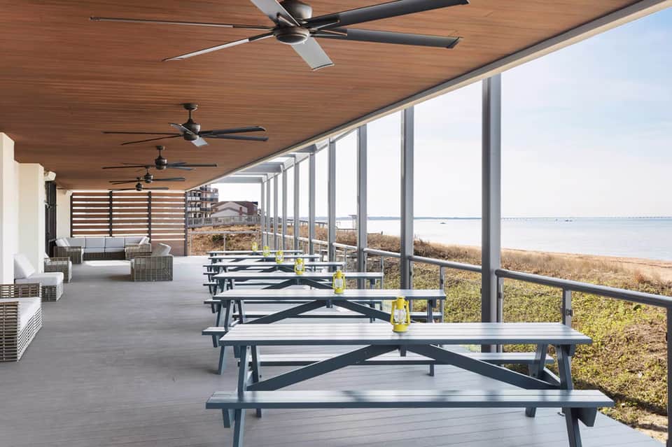 Covered seaside dining pavilion with picnic tables overlooking a beach and bay with ceiling fans