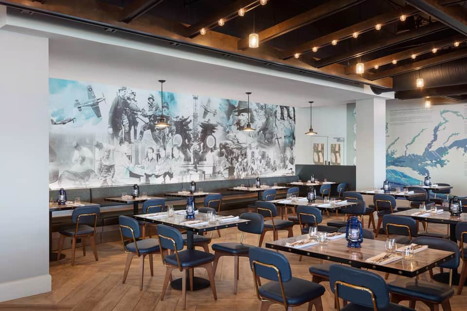 Modern conference room with blue chairs, wooden tables, and large wall mural featuring historical aviation imagery and maps