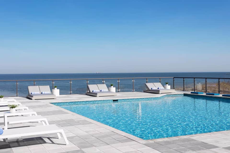 Oceanfront resort pool with lounge chairs and sea view under clear blue sky