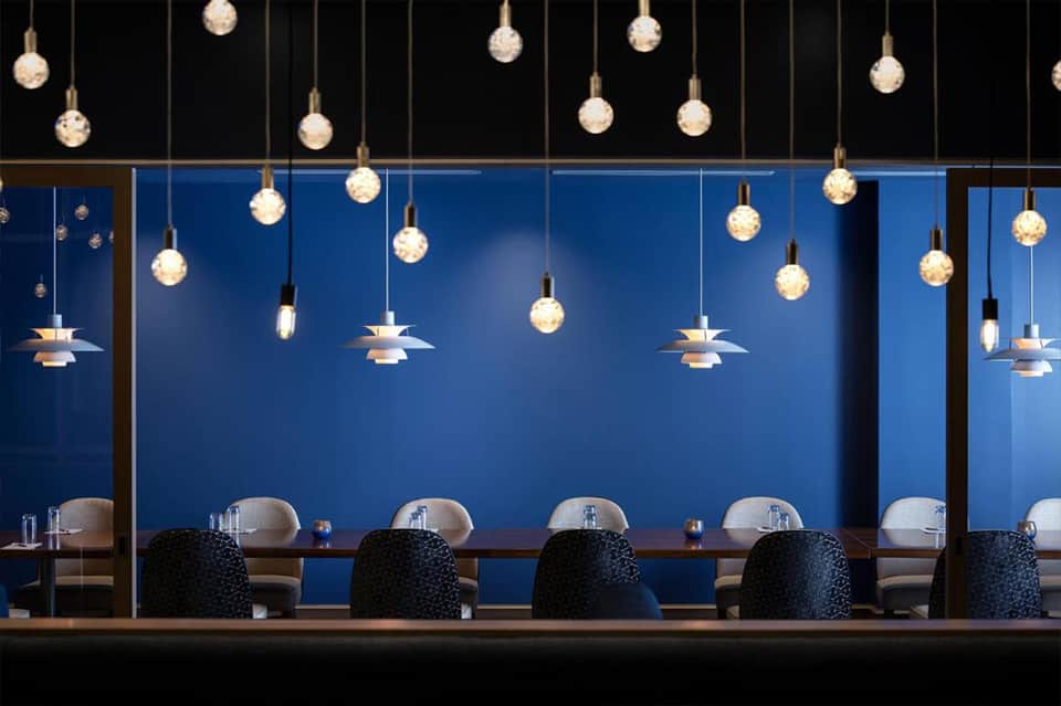 Modern fine dining restaurant with blue walls, pendant globe lights, and minimalist black chairs at counter