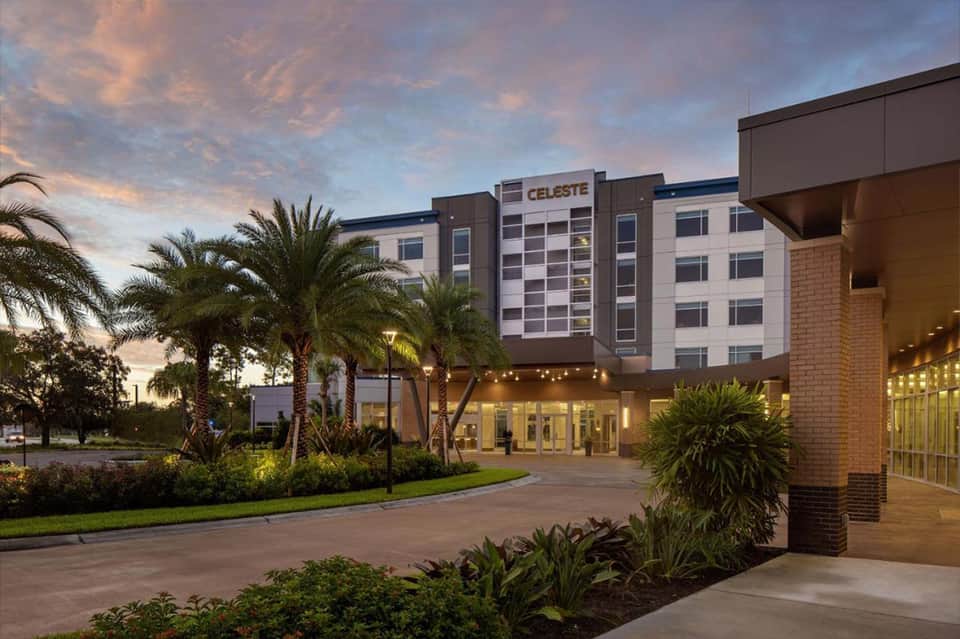 Hotel exterior at dusk with palm trees, brick facade, and illuminated entrance under purple sky