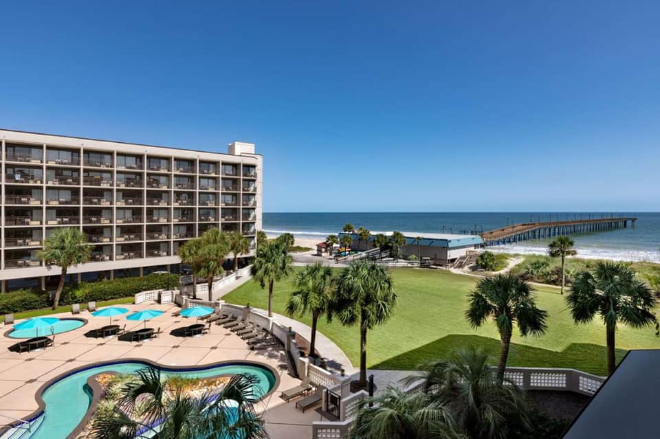 Beachfront high-rise resort with curved pool, palm trees, and pier view