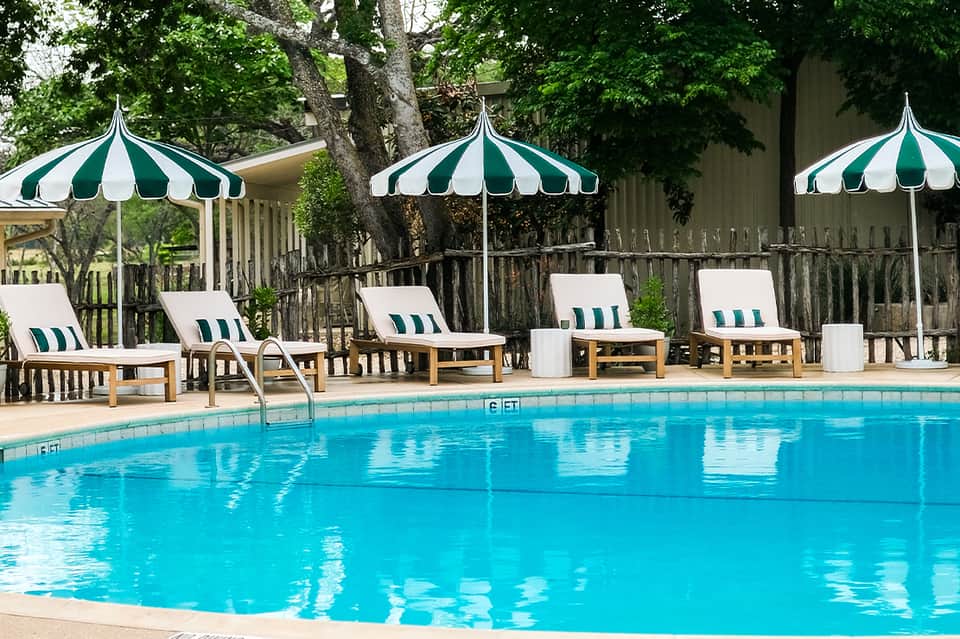 Resort pool with crystal blue water, green and white striped umbrellas, and wooden lounge chairs