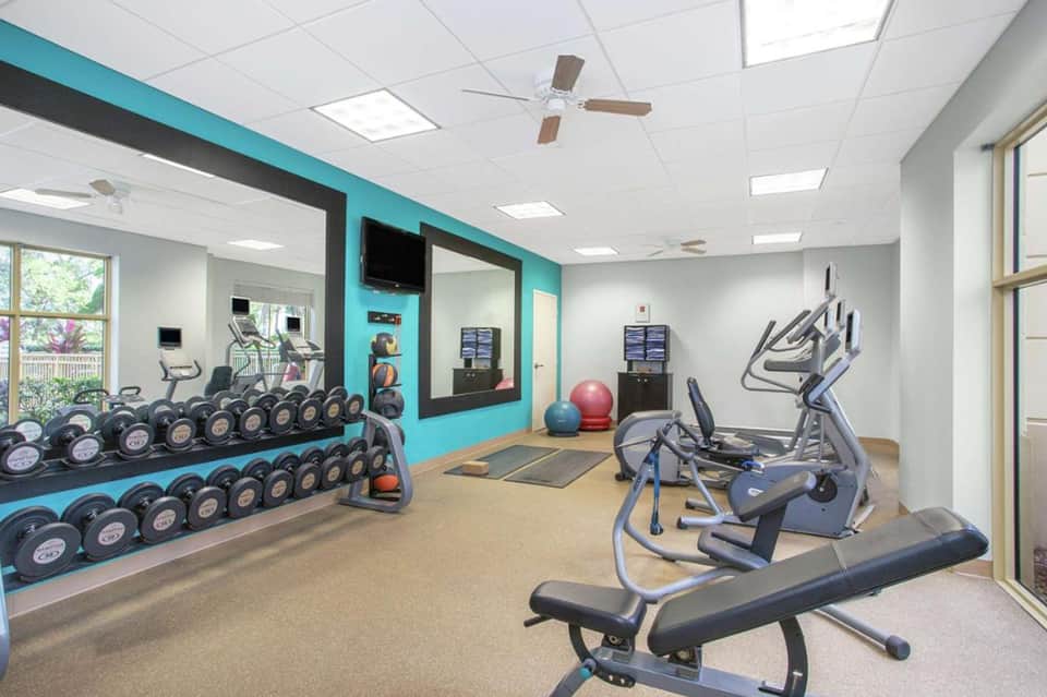 Bright fitness center with turquoise accent wall, dumbbell racks, cardio equipment, and mirrored workout space.